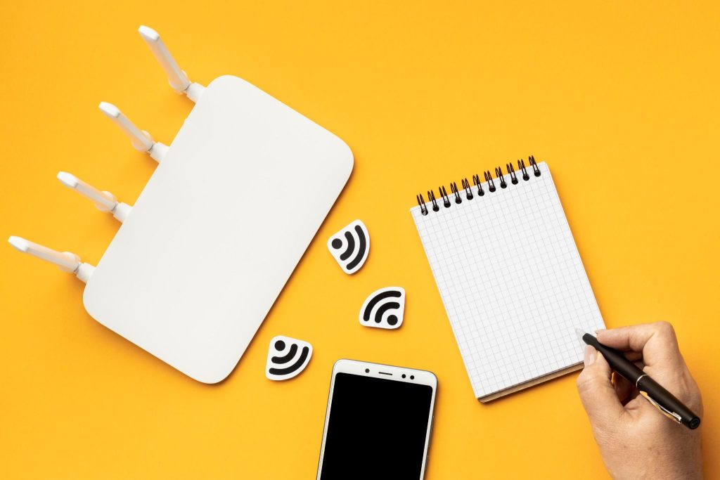 Roteador Wi-Fi, smartphone e bloco de anotações sobre fundo amarelo, simbolizando o planejamento para renegociar planos de internet e aplicar estratégias de como economizar mensalmente nas contas fixas.