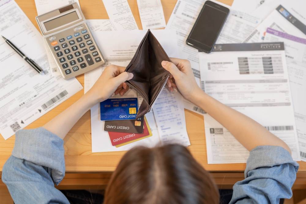 Pessoa organizando contas e anotações financeiras em uma mesa, com calculadora e caderno.