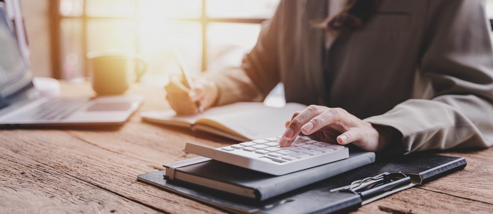 pessoa fazendo anotações e usando calculadora em mesa de trabalho para planejamento financeiro pessoal
