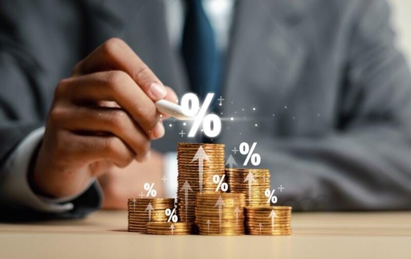 Pessoa de terno empilhando moedas com símbolos de porcentagem e setas de crescimento, representando lucros e juros em o que é renda fixa e renda variável.