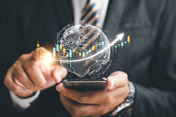 Homem de terno utilizando o celular enquanto gráficos financeiros em 3D e um globo virtual representam o crescimento dos investimentos, simbolizando o que é renda fixa e renda variável e a evolução no mercado financeiro.