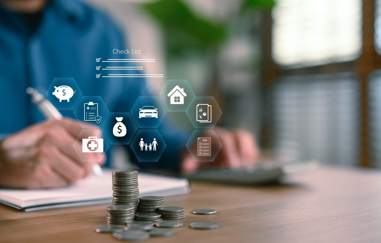 Pessoa fazendo anotações e usando calculadora ao lado de pilhas de moedas e ícones digitais de finanças, ilustrando como criar metas financeiras pessoais de forma organizada.