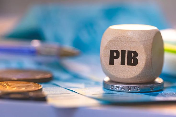 Imagem com moedas, cédulas brasileiras e um cubo de madeira com a sigla PIB, representando o conceito de o que é o PIB e por que ele é importante para a economia.